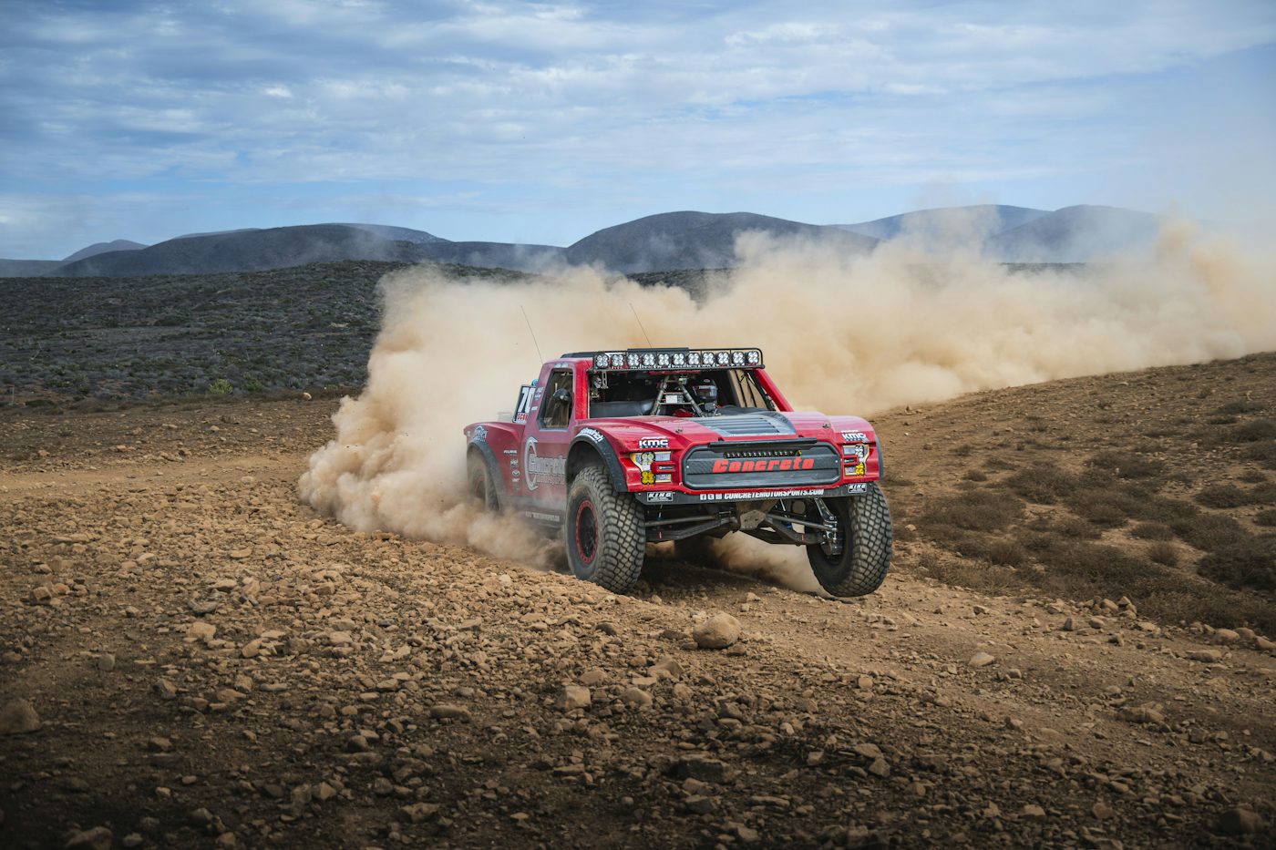 Off-road race truck kicking up dust on a desert track