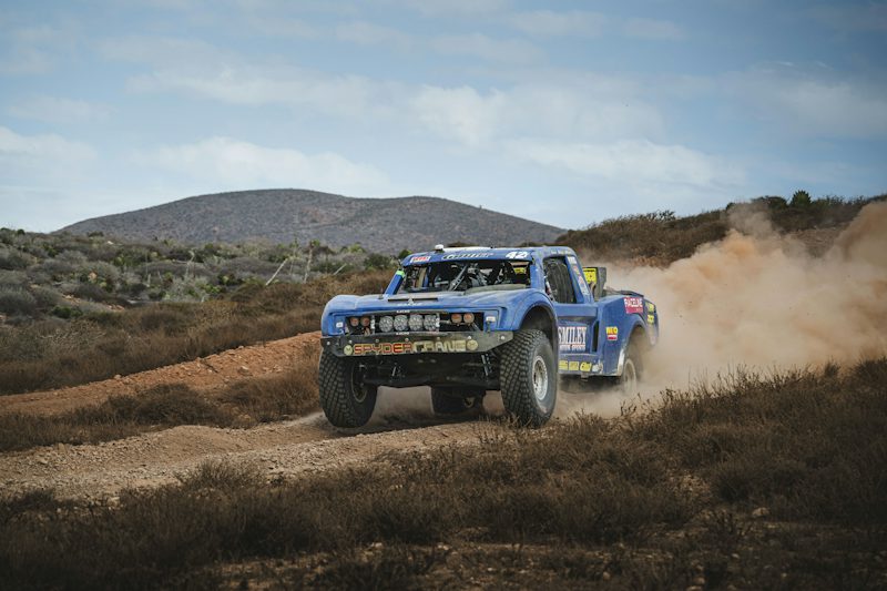 Blue off-road race truck raising dust on a dirt track