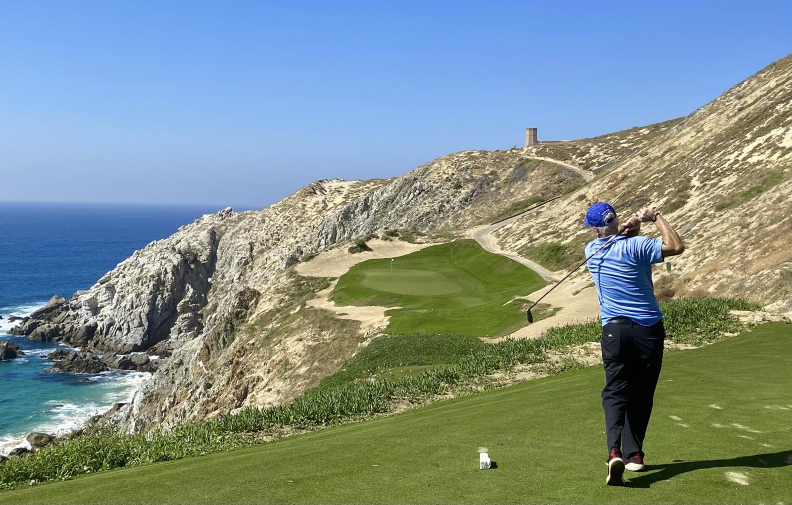 Golfer teeing off on a clifftop hole at Quivira, Los Cabos