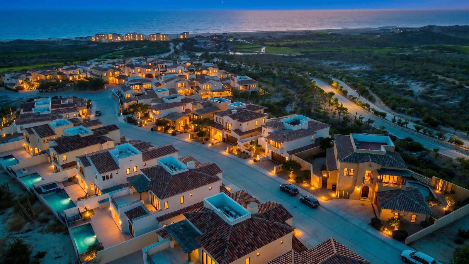 Aerial view of Rancho San Lucas at dusk, with its homes lit up and the Pacific Ocean on the horizon